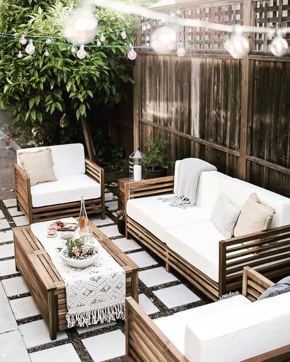 an outdoor space with wooden furniture in lighter colors, and rope light bulbs #backyard #backyarddesign #outdoordecor #outdoorliving  #backyardDecor #backayrd #backyardParty #outdoorPartyIdeas #patioFurniture #patiodecor #patio #backyardporch #backyardLighting #outdoorLights #lighting #lights #ropeLights #stringLights