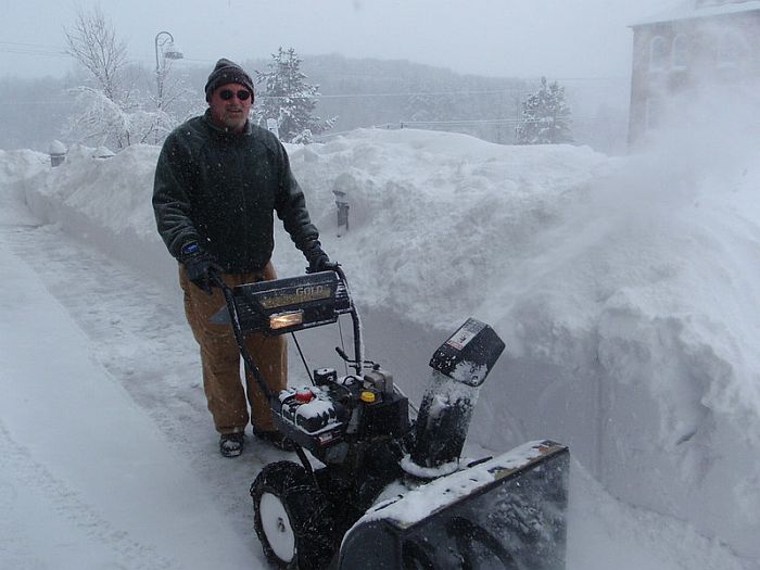 A man in winter clothes operating a gas snow blower