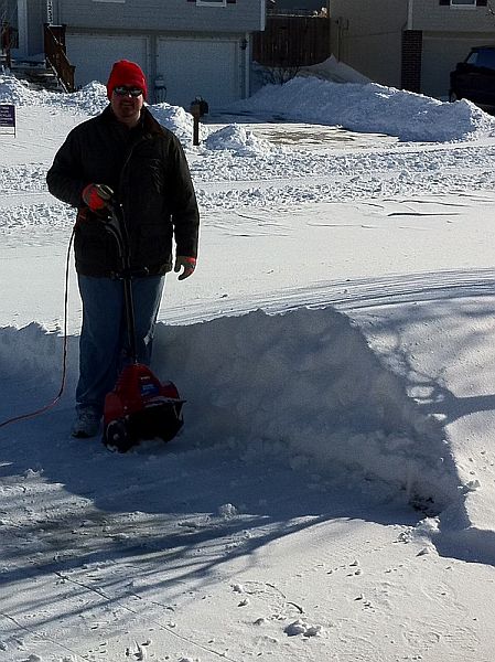 An adult man clearing some snow with an electric snow shovel