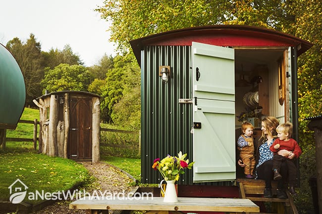Prefab small rustic container garden shed, and a woman with two small children seated on the step
