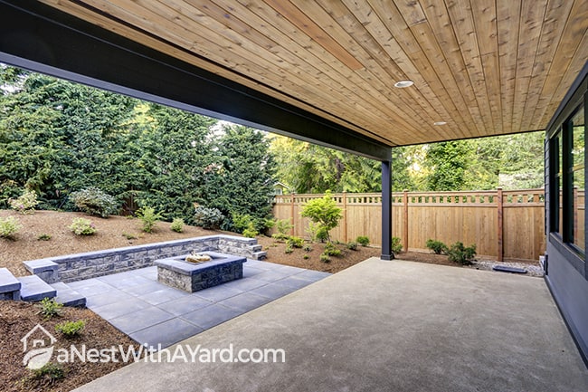New modern backyard garden patio covered with a timber plank ceiling and a rectangular fire pit, made of concrete and slate tiles.