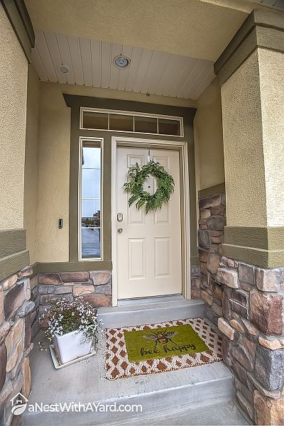 Porch decorated with spring wreath, potted plant and  door mat