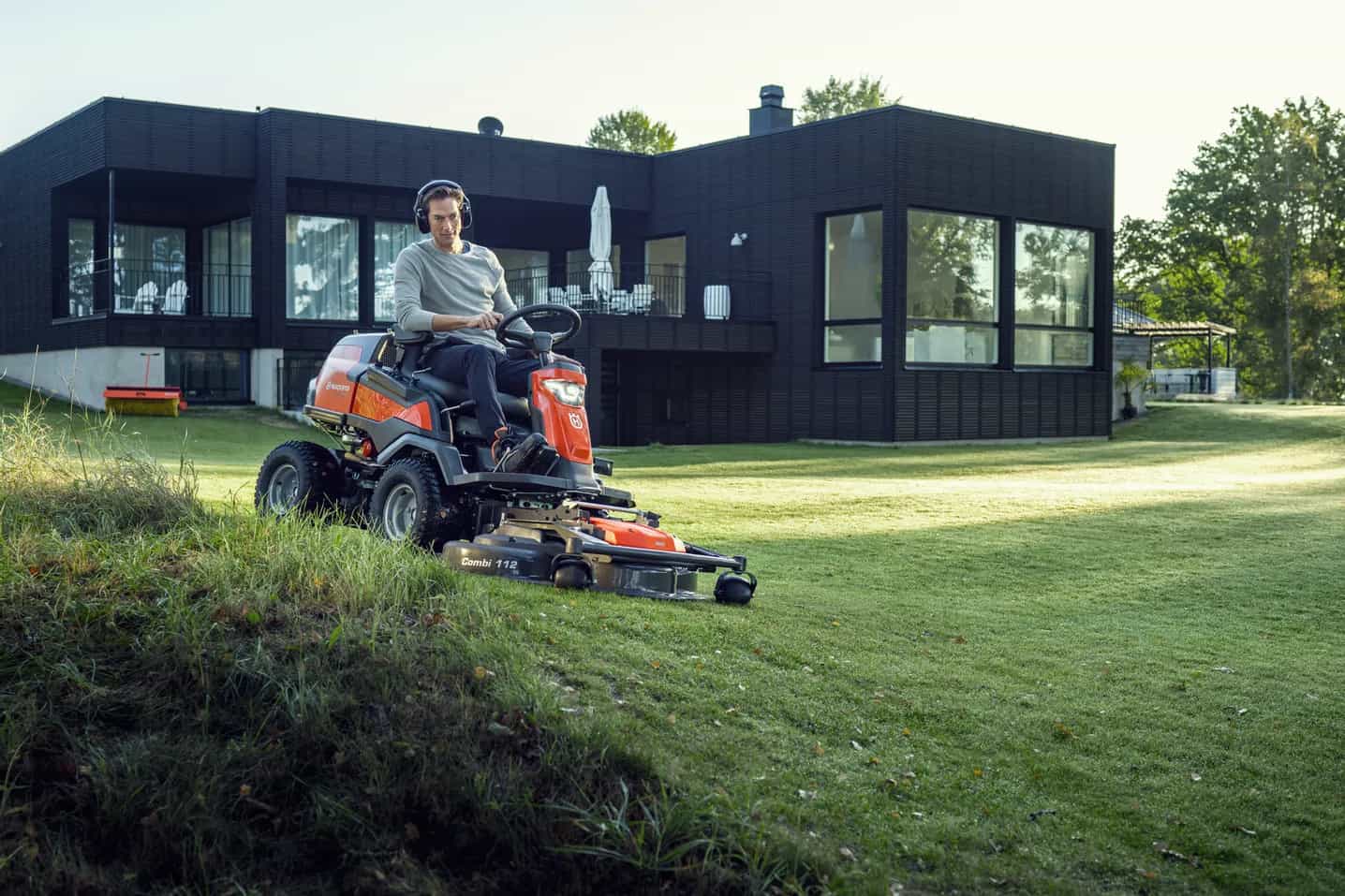 A man on headphones riding a lawnmower on a slightly curved yard.