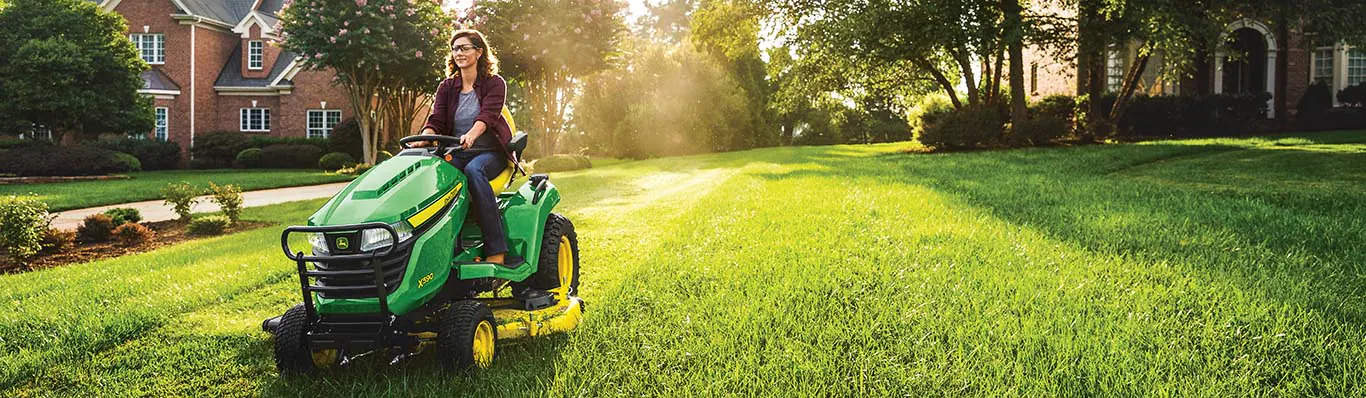 A woman driving a green lawnmower on a sunny morning.