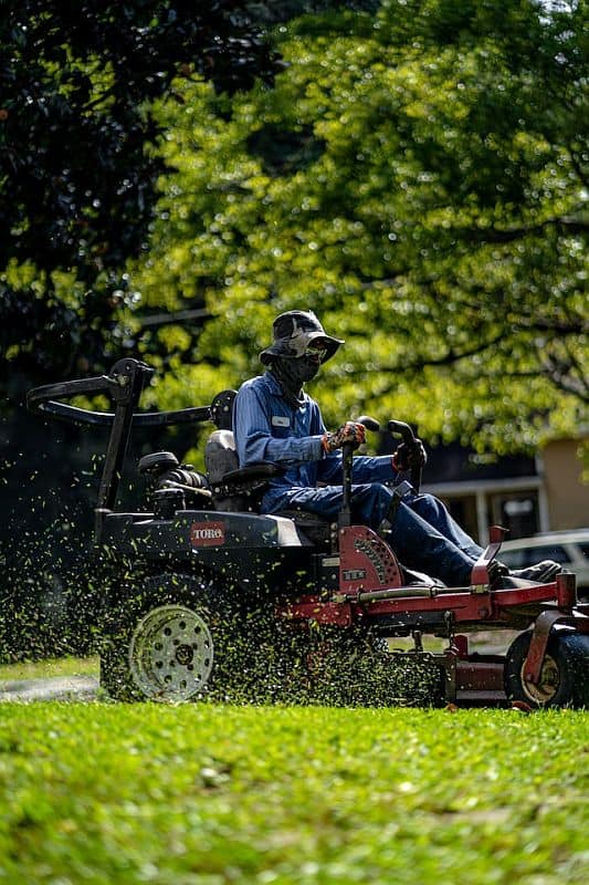 A uniformed person mowing a lawn with a big lawn mower