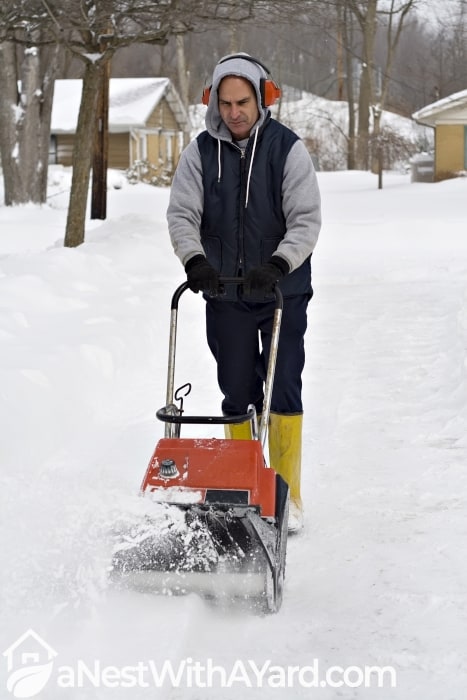 A man wearing ear protection clears his driveway with snowblowe