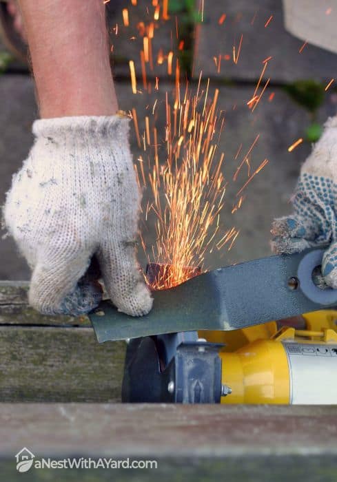 A man wearing safety gloves while sharpening a lawn mower blade