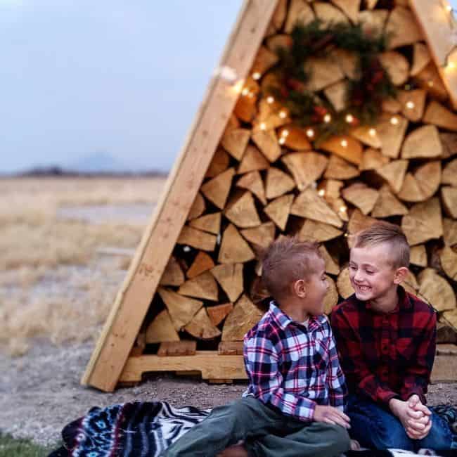 Kids sitting in front of a pyramid shape firewood storage