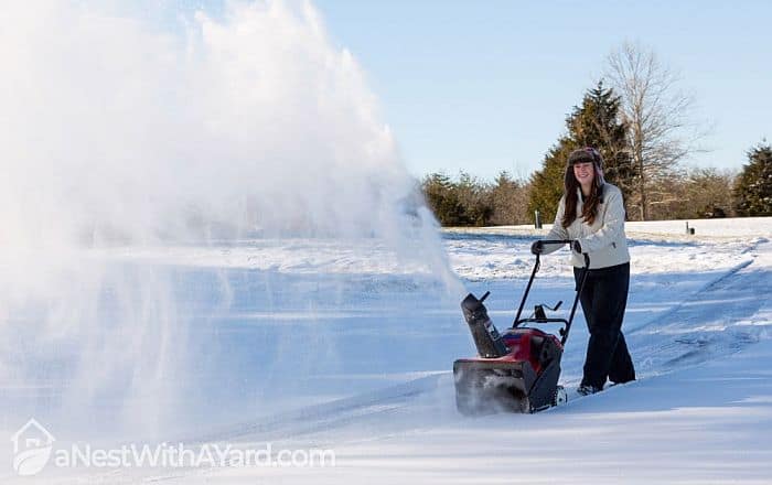 A woman operating a snow blower on her street